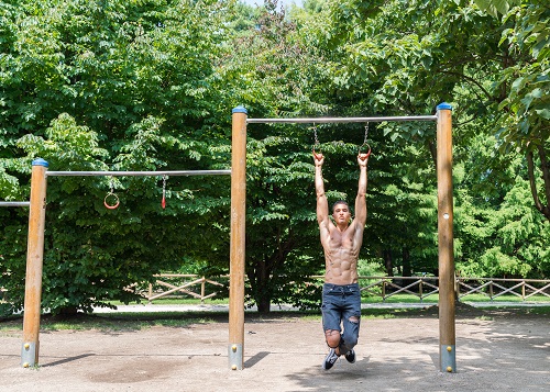 Young athletic shirtless man exercising on monkey bars in a park