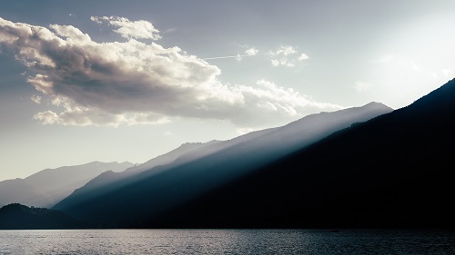 Clouds casting god rays on a diffused silhouette of Lake Como, Italy