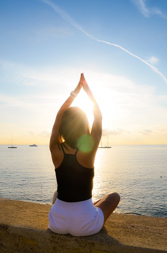 Young brunette woman (25-30) stretching while overlooking the sea in the Summer