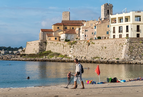 A man uses a metal detector on a beach overlooking Antibes, Cote d'Azur, France