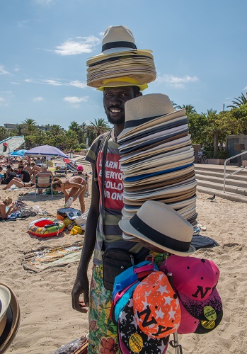 An African man sells straw hats on the beach in Antibes, France