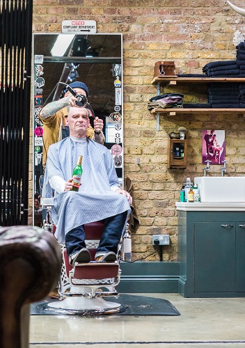 Hipster man drinking a beer having his hair cut in Shoreditch, London, England