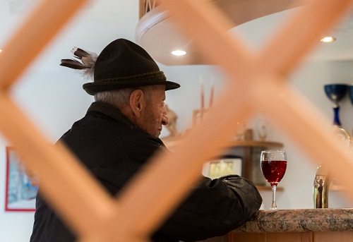 Old man with typical Austrian clothes drinks a red wine at a bar