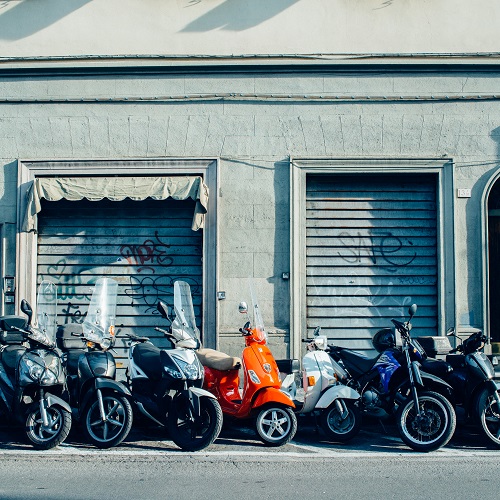 Red Italian vespa parked on street with other motorbikes