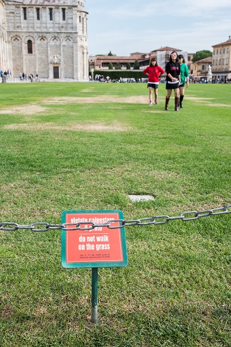 Asian tourists in Pisa, Italy disobey the sign to keep off the grass