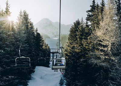 Sun through pine trees as chairlift ascent at Italian ski area covered in snow