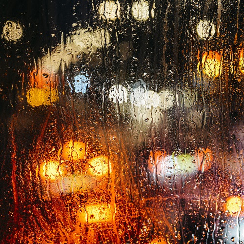 Emotional melancholic abstract background with defocused lights bokeh in London, UK behind rain drops in window glass, Focus on few drops due to the shallow depth of field