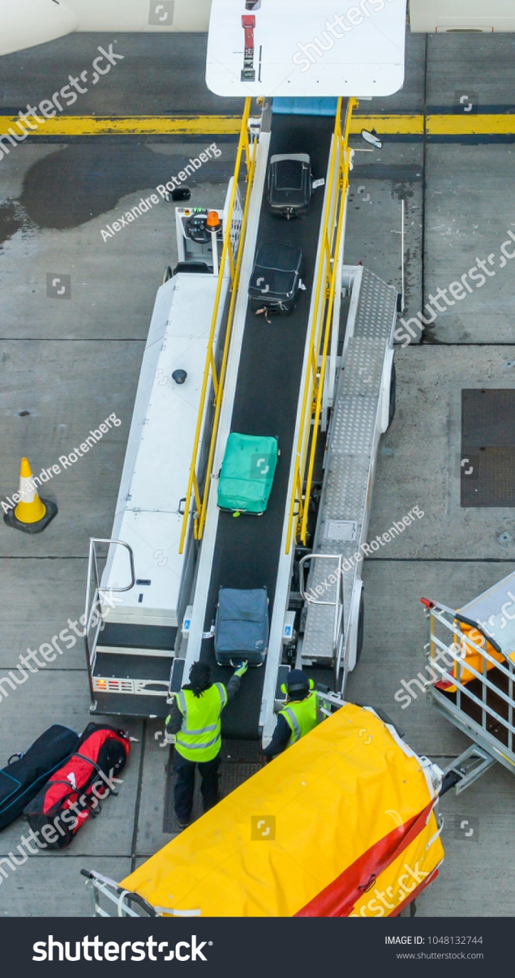 stock-photo-high-perspective-of-unidentifitable-baggage-handlers-picking-up-suitcases-from-a-conveyor-belt-1048132744