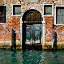 Facade of partially mossy old brick house with wooden vintage door on narrow canal in Venice, Italy.