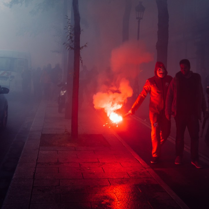 Protestors wearing a Guy Fawkes mask light gas canisters to express their anger against French President Macro's government, among other issues, on the streets of Paris