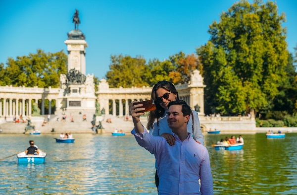 Couple takes a selfie in front of boats across from monument to Alfonso XII in the Parque del Buen Retiro, Madrid, Spain
