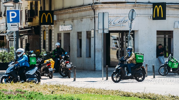 Glovo and UberEats delivery couriers on motorbike in front of a McDonalds restaurant during the Coronavirus Covid-19 outbreak